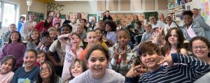 Smiling students in MTE#2’s Mrs. Robinson and Mr. Mallon’s classes gathered in a crowd for a photo after they received a special visit from Lauren Keating-Wear, the mother of Kanen Keating-Wear, for World Kindness Day.