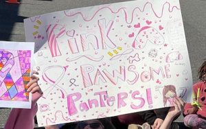 Fourth grader Cassidy Moore holding her handmade paper sign that reads “Pink Pawsome Panthers” for breast cancer awareness.