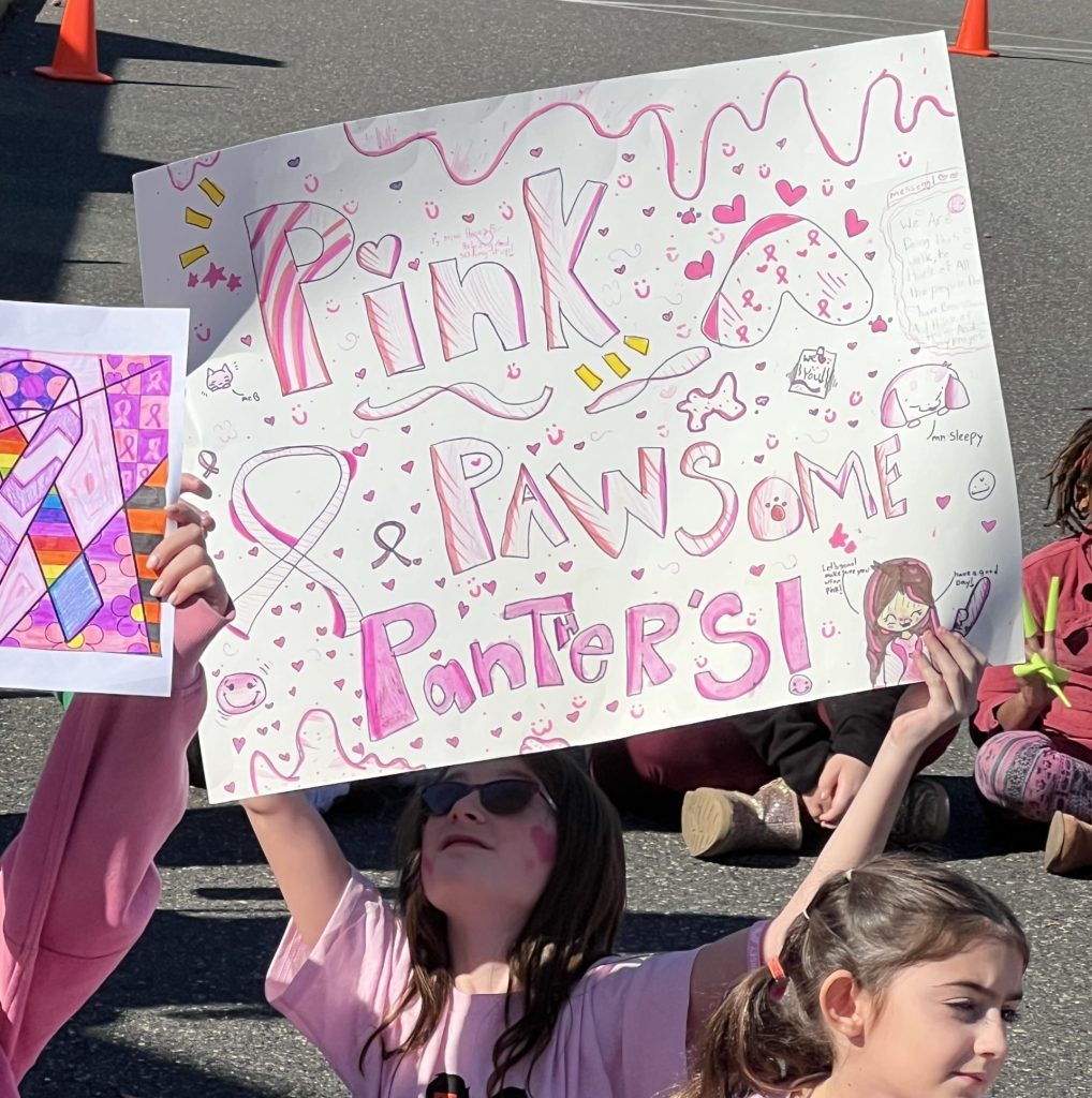 Fourth grader Cassidy Moore holding her handmade paper sign that reads “Pink Pawsome Panthers” for breast cancer awareness.