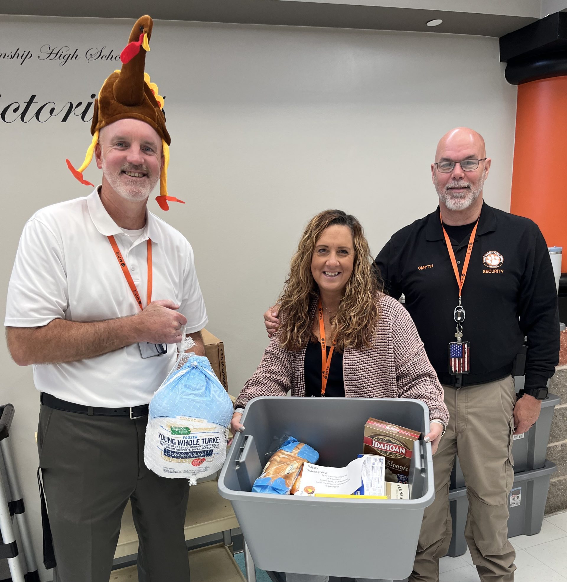 Three Middle Township School Teachers and Staff standing holding thanksgiving donations like a turkey and other food 