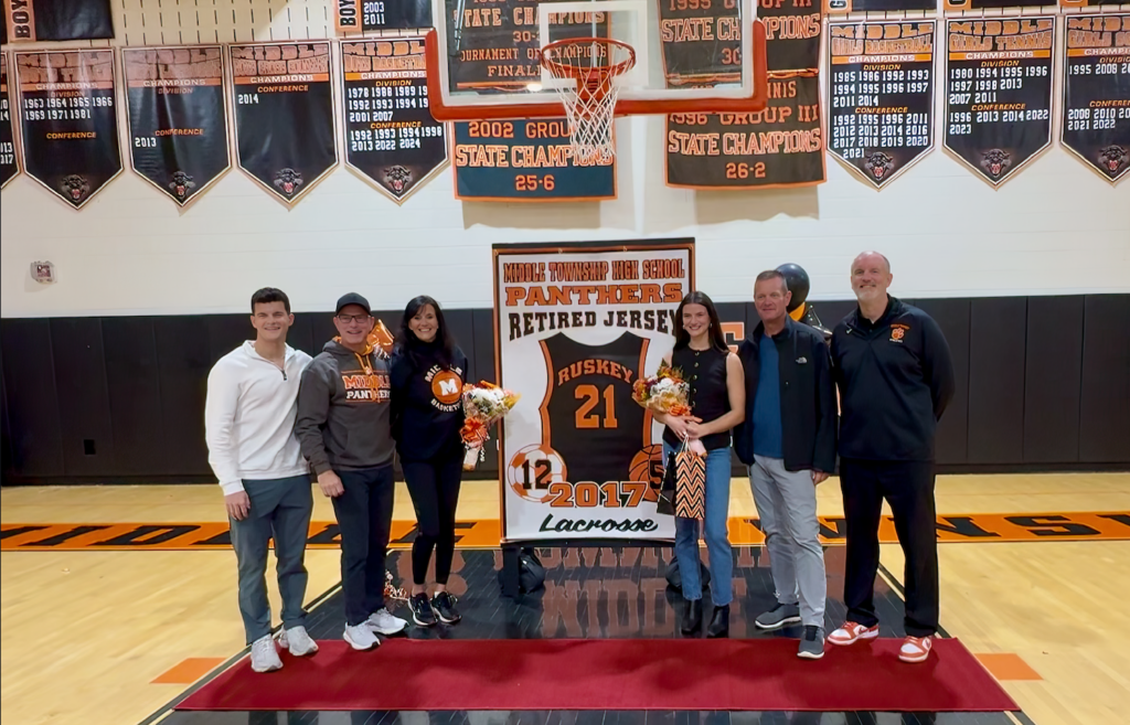 Bridget Ruskey standing with her family and former coaches in front of her jersey retirement banner - which will be hung in the MTHS gymnasium. 