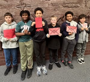 Six MTE#2 fifth-graders holding up handmade Valentine's Day cards.